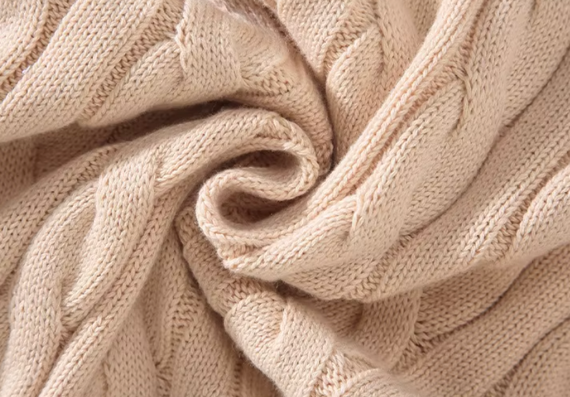 Close-up of the chunky cable knit texture of a men's beige half-zip sweater