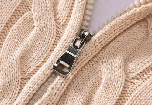 Close-up of the metal zipper pull on a men's beige cable knit half-zip sweater